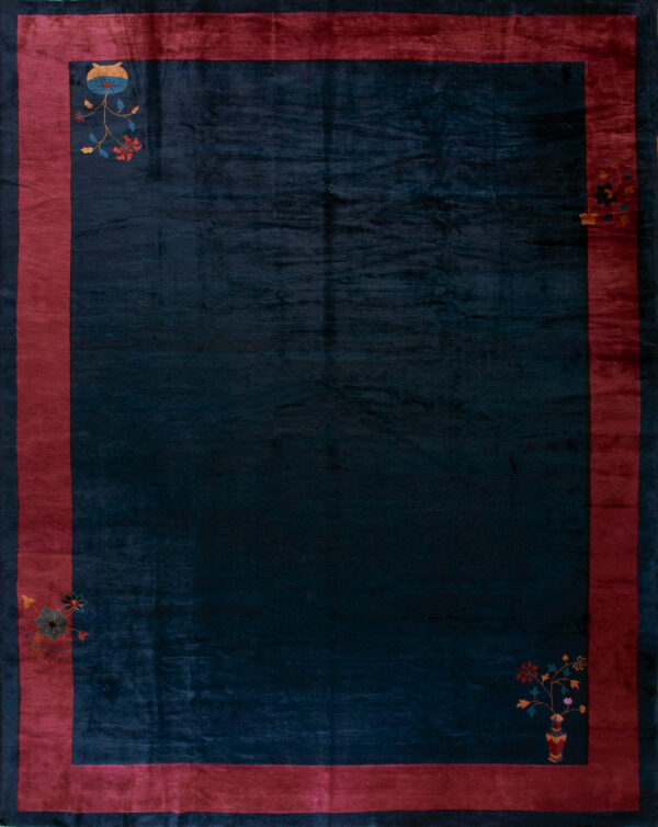 Plush dark blue rug with a magenta border featuring small colorful floral corner designs on wood.