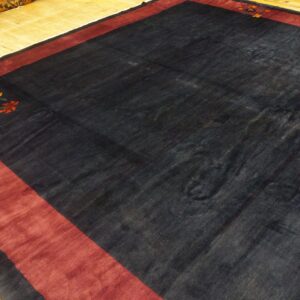 A dark field rug with a wide red border and a stylized floral corner motif rests on wood planks.
