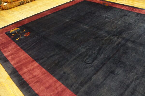 A dark field rug with a wide red border and a stylized floral corner motif rests on wood planks.