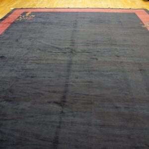 Large navy rug with broad red borders and colorful floral corner designs rests on polished wood flooring.