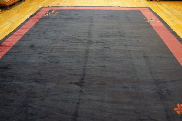 Large navy rug with broad red borders and colorful floral corner designs rests on polished wood flooring.