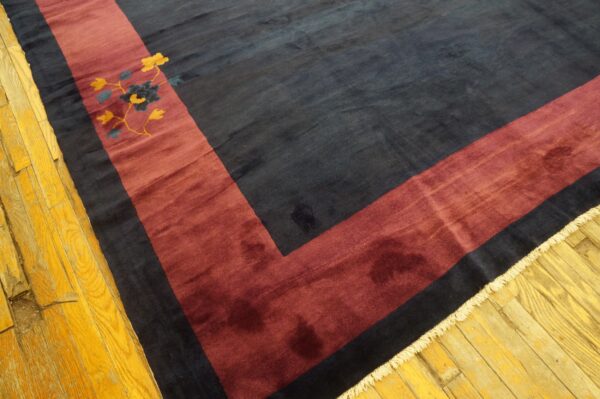 Plush dark blue rug with a maroon corner border and yellow floral detail on golden hardwood floors.