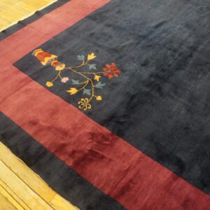Dark blue rug with a wide maroon border and colorful floral vase motif on light wood floor.