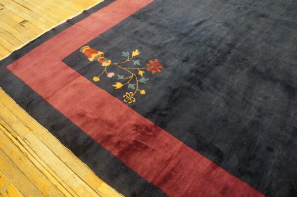 Dark blue rug with a wide maroon border and colorful floral vase motif on light wood floor.