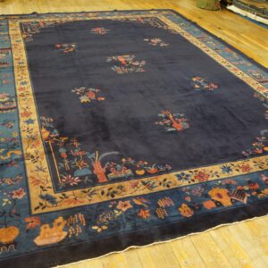 Dark blue rug with multi-colored flowers and vases has wide teal and tan decorative borders on wood flooring.