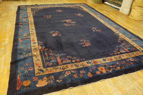 Dark blue rug with multi-colored flowers and vases has wide teal and tan decorative borders on wood flooring.