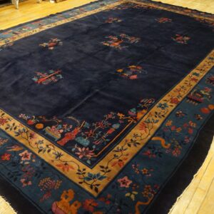 A large, navy blue rug with scattered multicolored floral motifs and intricate teal and gold borders rests on yellow wood flooring.