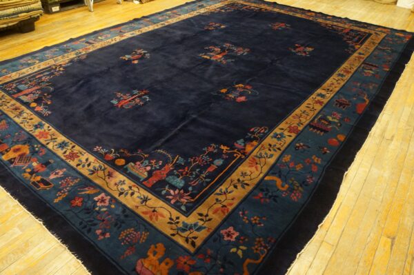 A large, navy blue rug with scattered multicolored floral motifs and intricate teal and gold borders rests on yellow wood flooring.