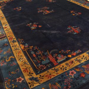Dark blue rug with scattered colorful botanical motifs and wide gold and teal borders on yellow wood floors.