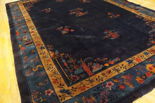 Dark blue rug with scattered colorful botanical motifs and wide gold and teal borders on yellow wood floors.
