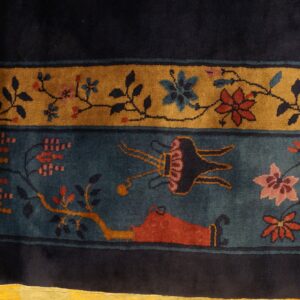 High-pile rug featuring indigo, gold, and teal borders with intricate red and pink botanical patterns on wood flooring.