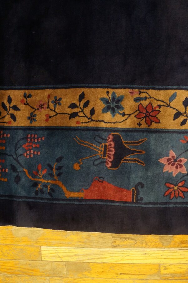 High-pile rug featuring indigo, gold, and teal borders with intricate red and pink botanical patterns on wood flooring.