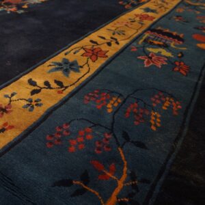 Plush rug detail showing navy, gold, and teal borders with detailed floral and vine patterns over wood flooring.