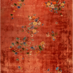 Low pile rug with a reddish-orange field showing abrash and scattered multicolor floral and leaf clusters.