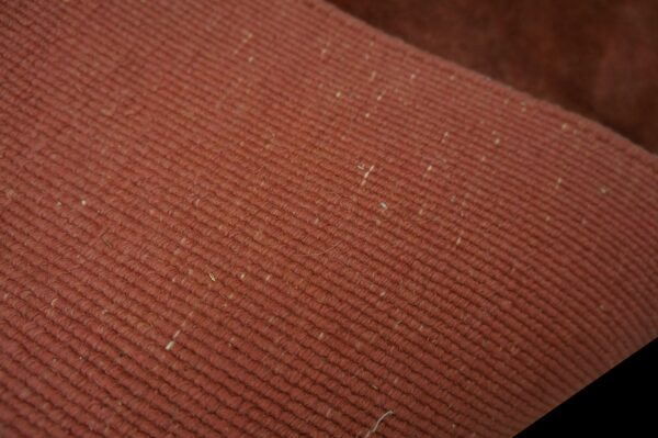 Reddish-brown rug detail showing parallel diagonal ribs and scattered light-colored inclusions.