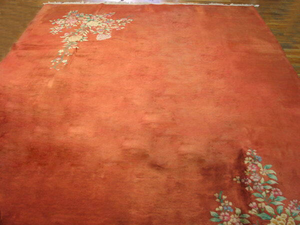 Orange high-pile area rug with soft floral corner accents displayed on dark wood flooring.