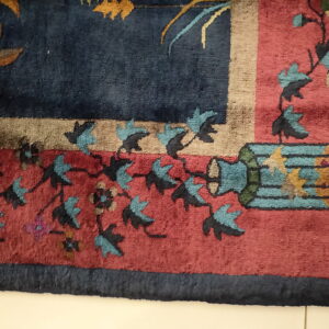 Close-up of a floral rug corner featuring navy, red, teal, and tan colors on a light tile floor.