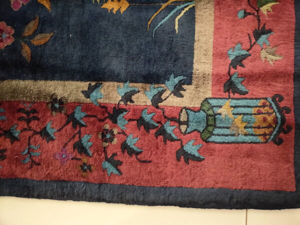 Close-up of a floral rug corner featuring navy, red, teal, and tan colors on a light tile floor.