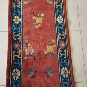 Dusty red runner with yellow, blue, and cream floral patterns and a dark blue border on white tile.