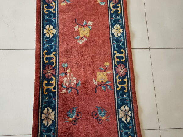 Dusty red runner with yellow, blue, and cream floral patterns and a dark blue border on white tile.