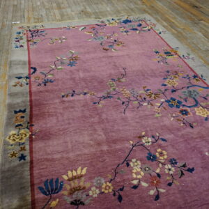 A mauve rug with a multicolor floral pattern and gray border rests on worn wooden plank floors.