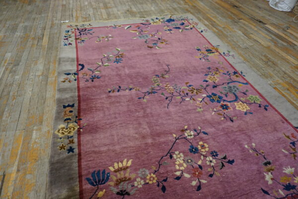 A mauve rug with a multicolor floral pattern and gray border rests on worn wooden plank floors.