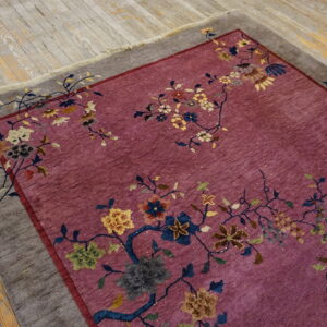 Pink floral rug with a gray border rests on distressed light wood plank flooring.