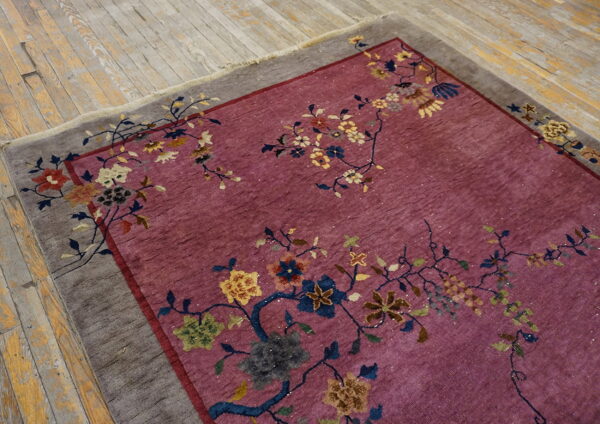 Pink floral rug with a gray border rests on distressed light wood plank flooring.