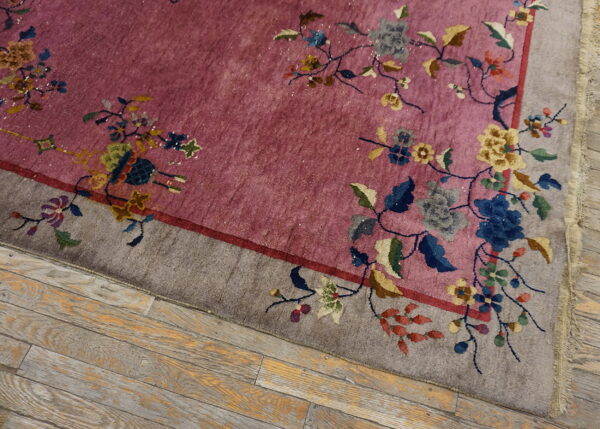 Rose field rug with flowing floral vines and a gray border rests on distressed wood planks.