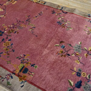 Dusty pink rug with a wide gray border and sprawling, multicolored floral and vine motifs on wood flooring.