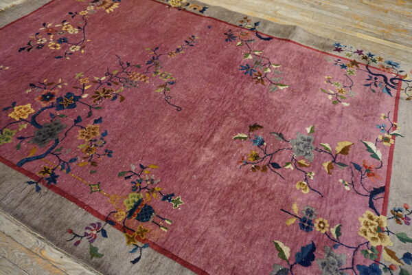 Dusty pink rug with a wide gray border and sprawling, multicolored floral and vine motifs on wood flooring.