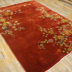 High-sheen rust rug with colorful floral sprays rests on unfinished light wood floorboards.