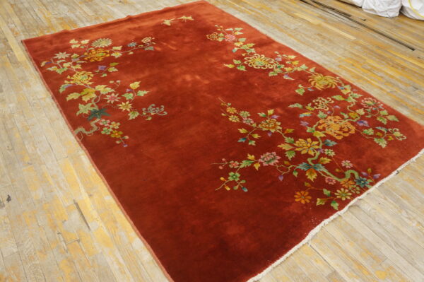 High-sheen rust rug with colorful floral sprays rests on unfinished light wood floorboards.