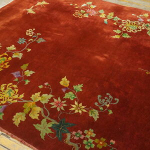 Reddish-brown rug with sprawling yellow and green floral borders on a light distressed wood floor.