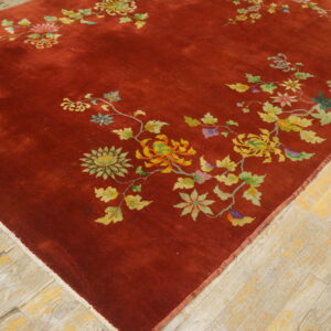 Angled view of a deep red rug featuring multicolored flowers and butterflies on light, distressed wooden floors.
