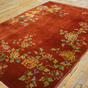 A low-pile rust rug featuring a detailed multicolored floral and vine pattern lies on distressed light wood floors.