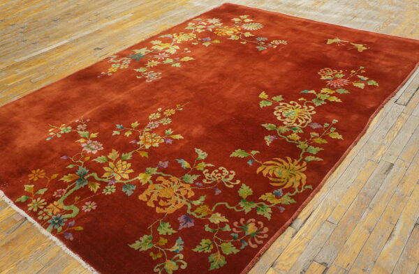 A low-pile rust rug featuring a detailed multicolored floral and vine pattern lies on distressed light wood floors.