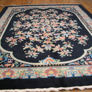 Plush navy rug displays a large botanical pattern in pastel pinks and greens on hardwood flooring.