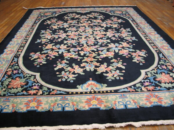 Plush navy rug displays a large botanical pattern in pastel pinks and greens on hardwood flooring.