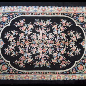 Black rug featuring a blossoming tree design in pink, blue, and green within an ornate central medallion.