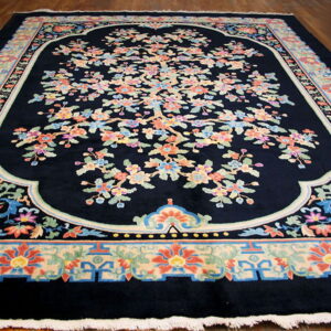Plush dark blue rug with a central scalloped medallion and colorful floral tree design on wood floors.