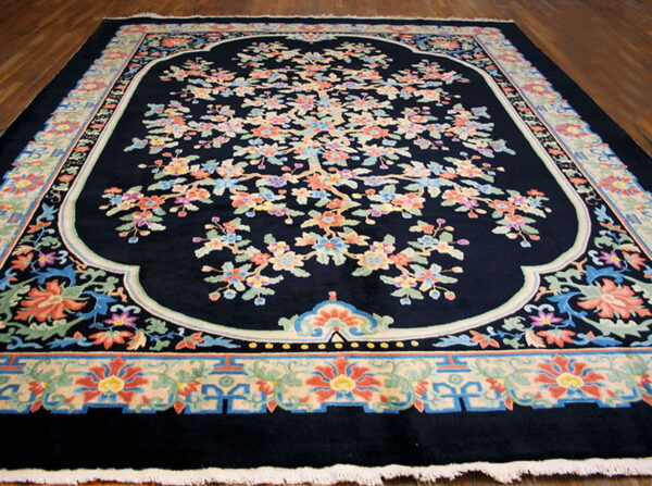 Plush dark blue rug with a central scalloped medallion and colorful floral tree design on wood floors.