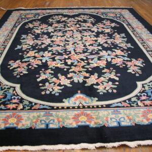 Large dark blue rug featuring a central multicolored flowering tree design and wide pastel borders on wood flooring.