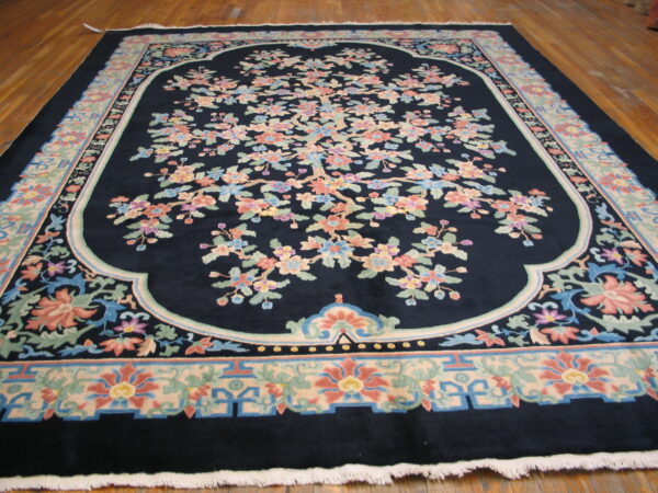 Large dark blue rug featuring a central multicolored flowering tree design and wide pastel borders on wood flooring.
