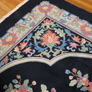 Navy rug with intricate pink, blue, and green floral and geometric borders shown on wood flooring.