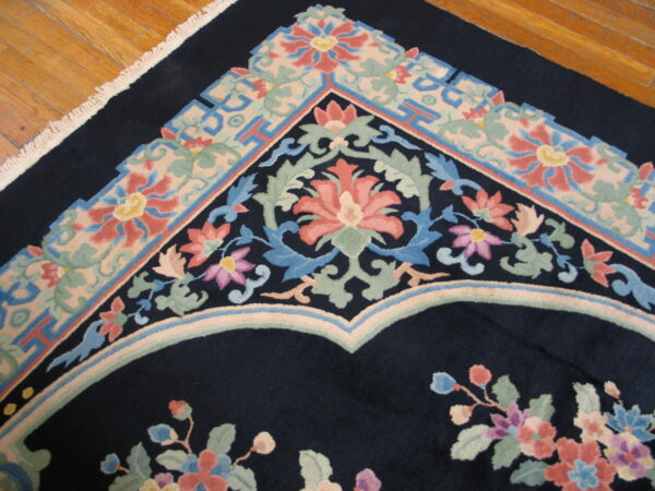 Navy rug with intricate pink, blue, and green floral and geometric borders shown on wood flooring.