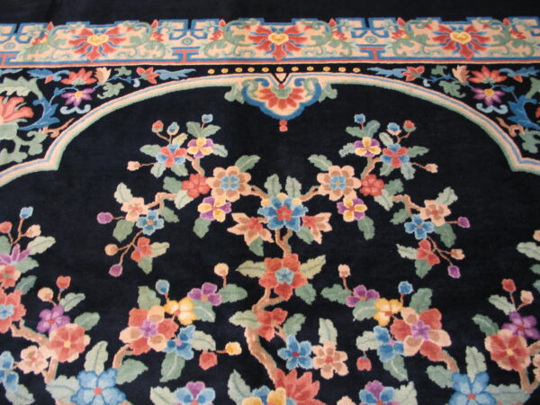 Plush navy rug detail showing colorful floral branches within an arched frame and geometric borders.