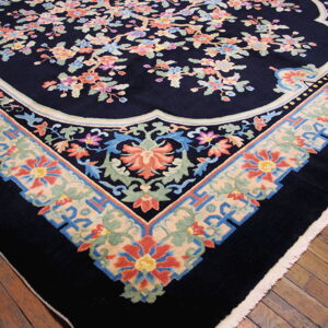 Navy rug featuring colorful flowering branches and a wide scalloped border rests on glossy wood flooring.