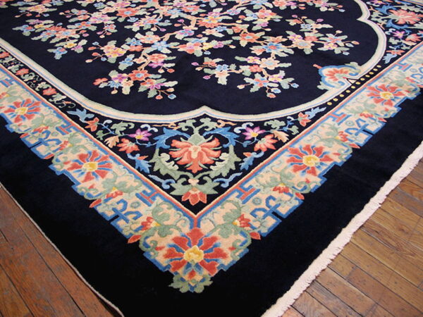 Navy rug featuring colorful flowering branches and a wide scalloped border rests on glossy wood flooring.