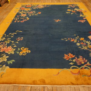 Floral rug with a blue field and yellow border lays on wide plank wooden floorboards.